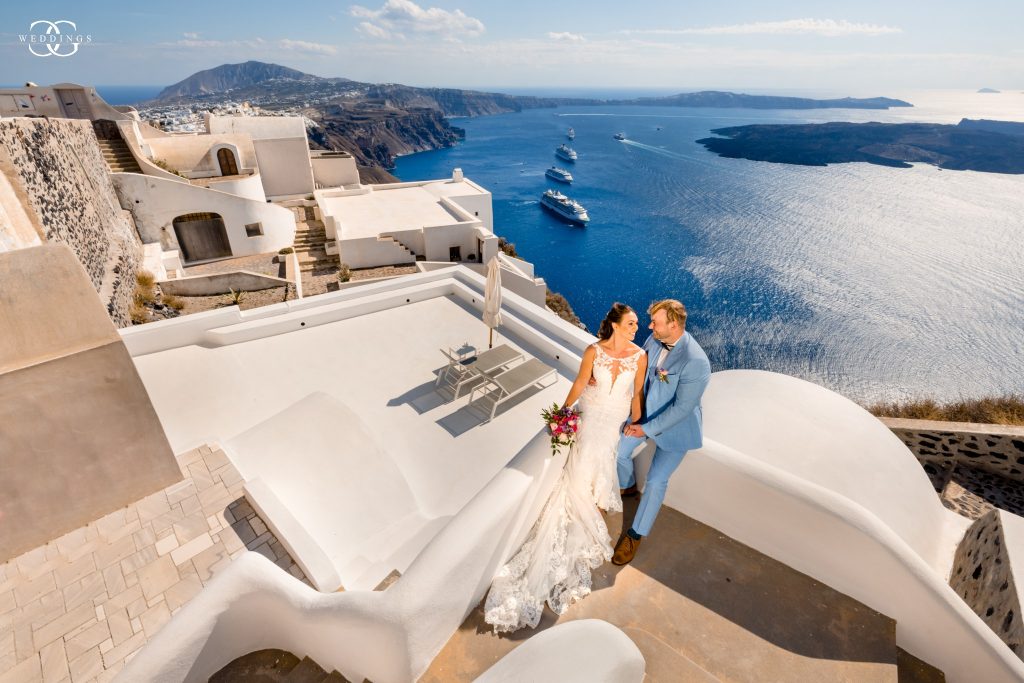 bride and groom sitting on the edge of a building overlooking the famous santorini caldera