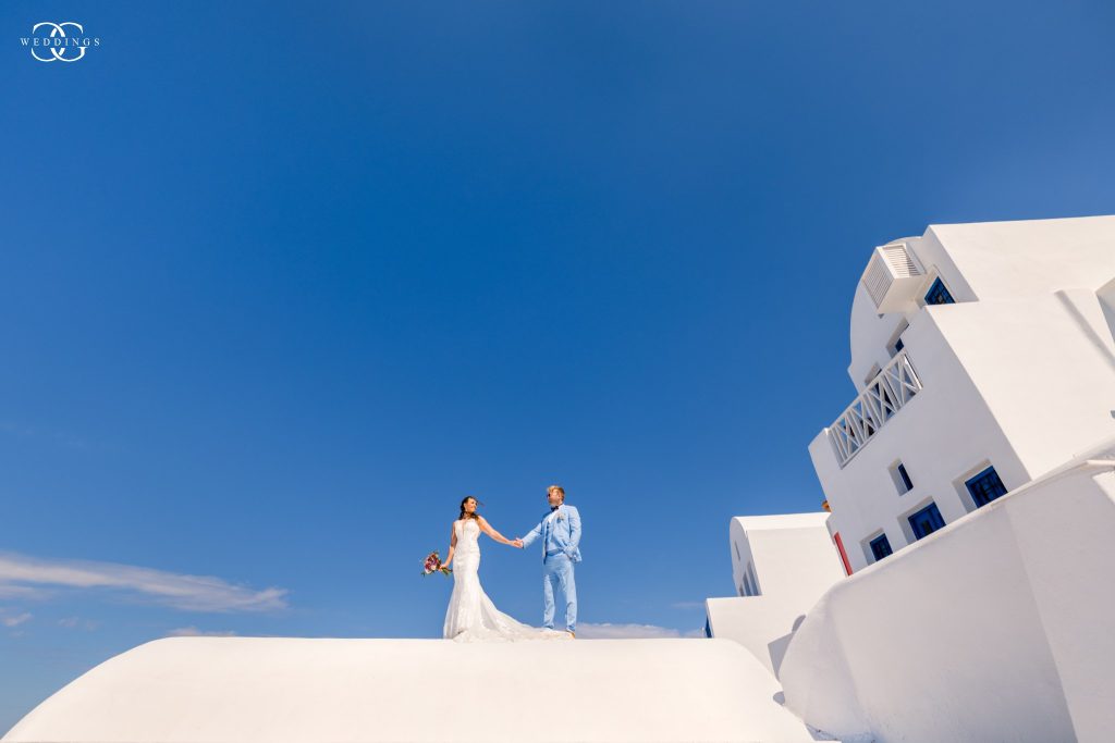 Bride and groom is standing on top of white-washed building in Santorini for their destination wedding photo
