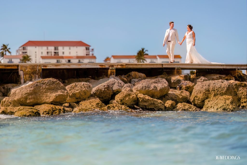 bride and groom walking on a pier in the sea during their destination wedding in Bahamas with blue sky backdrop while photographed by CG Weddings