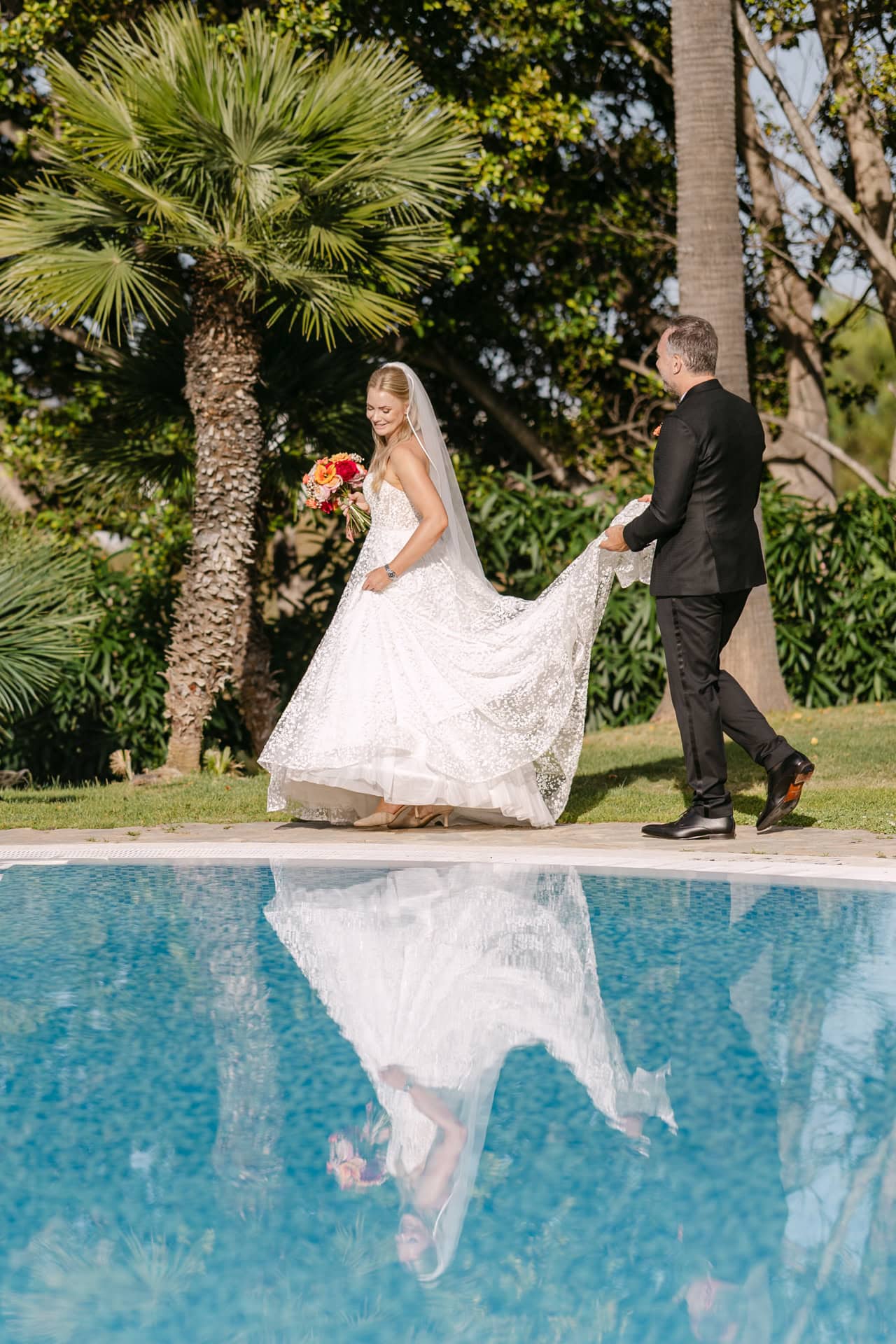 Bride and groom walking beside pool