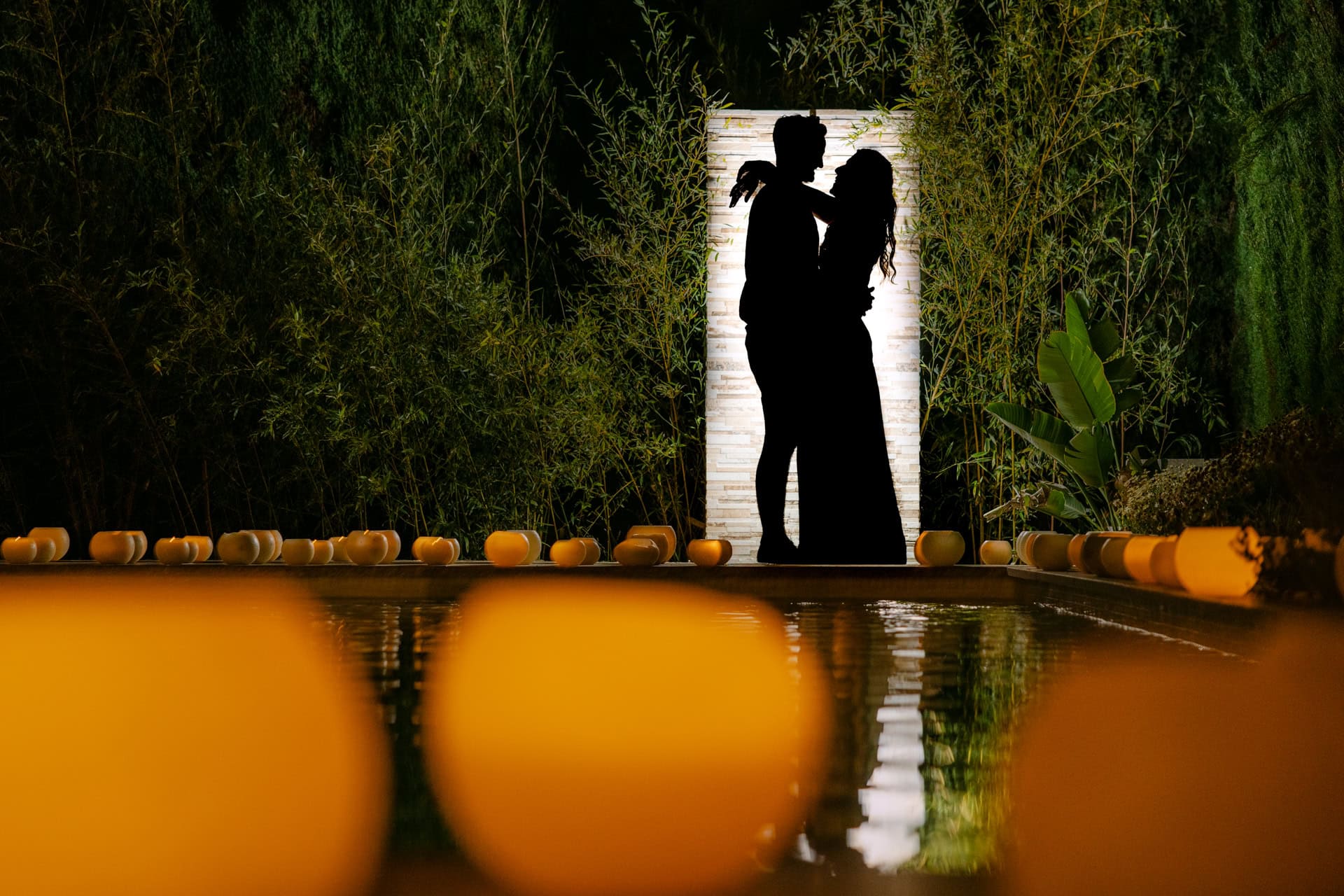 Silhouetted couple embracing by candlelit pool at night