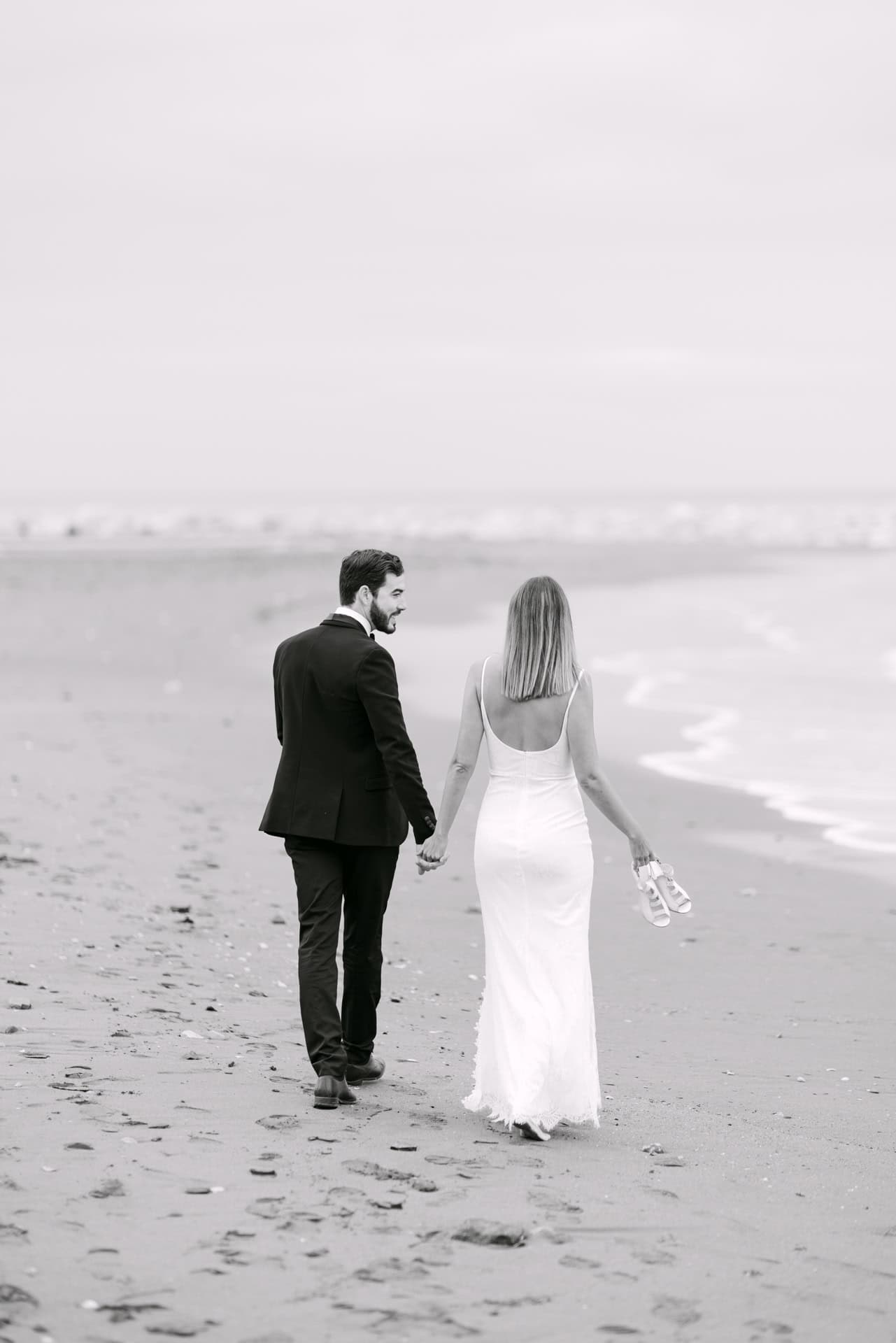 Couple holding hands walking along sandy beach in Marbella during their wedding photography portrait session
