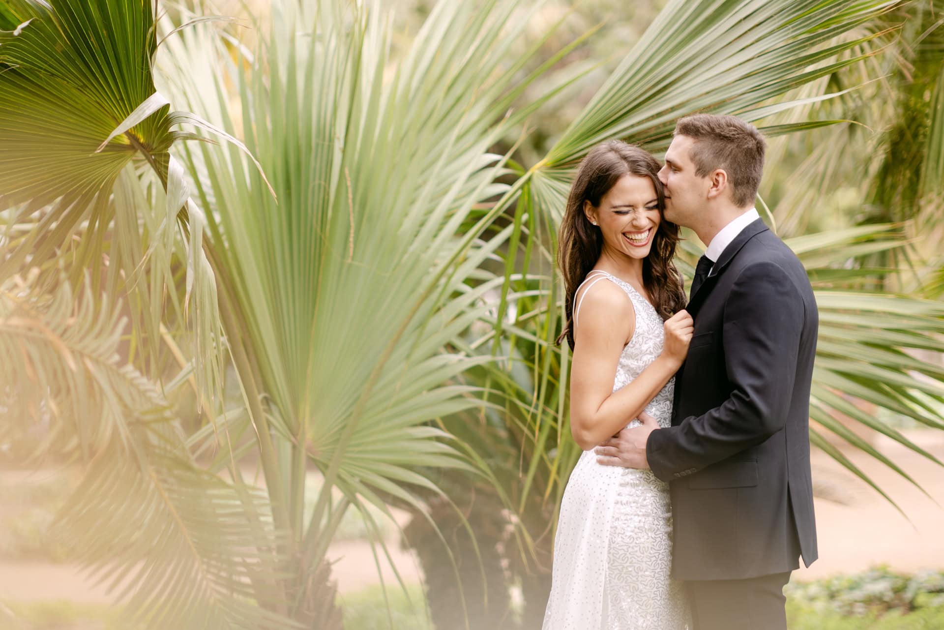 Bride and groom embracing among tropical palm leaves