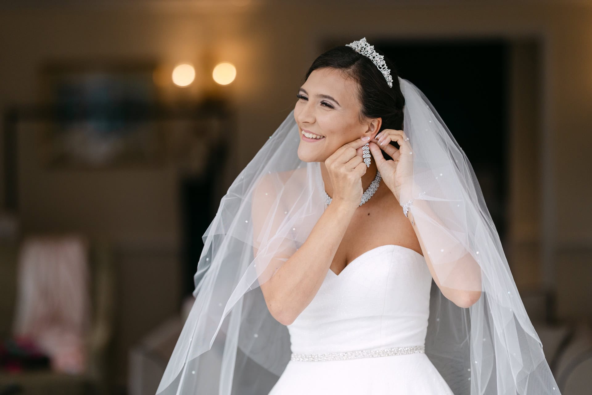 Bride adjusting earrings beneath wedding veil