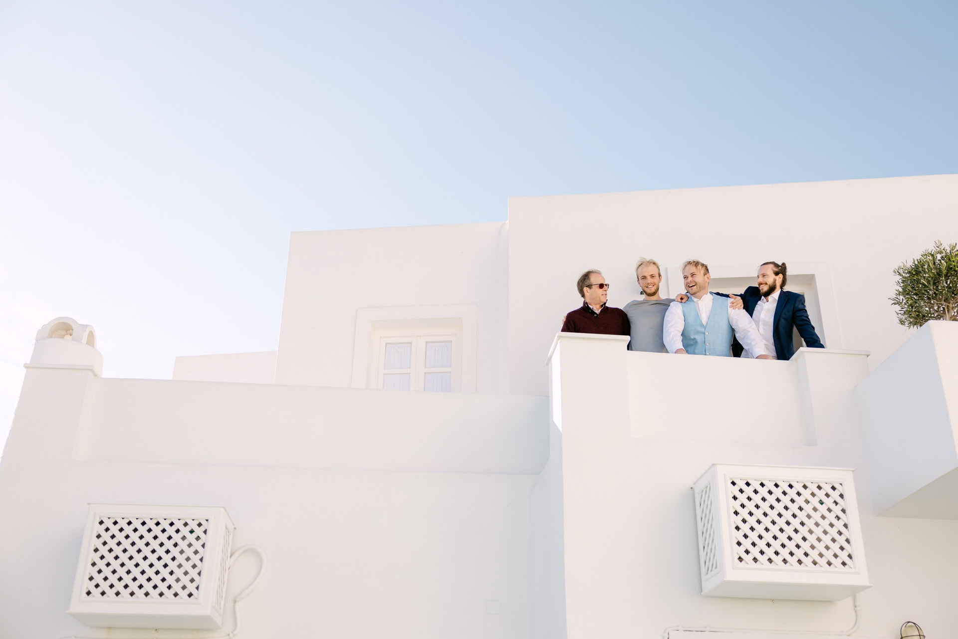 Four men smiling on white balcony