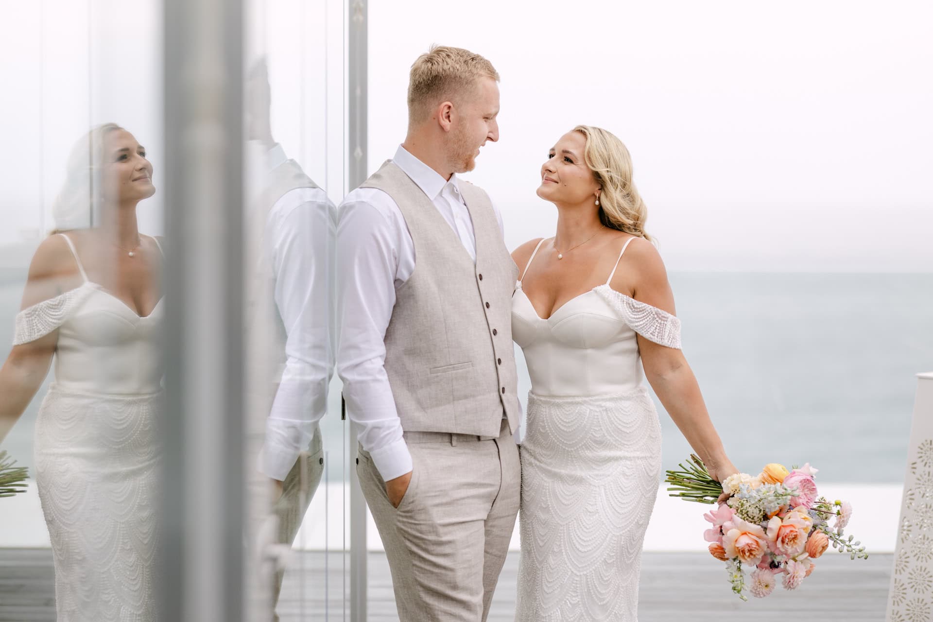 Bride and groom smiling by seaside window