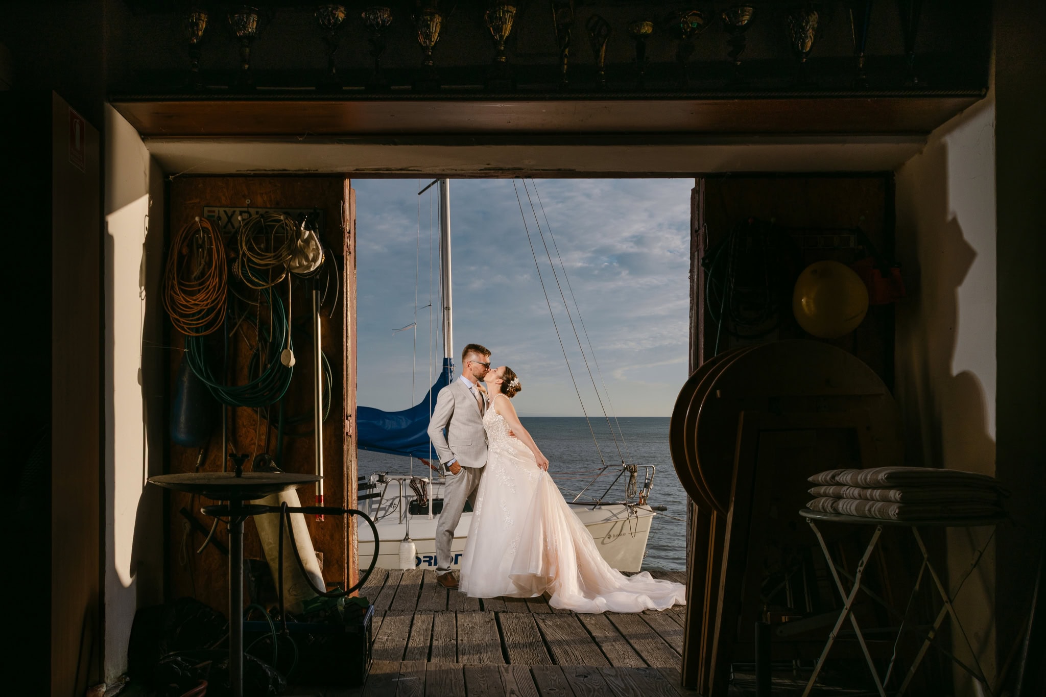 Bride and groom kissing by sailboat at sunset