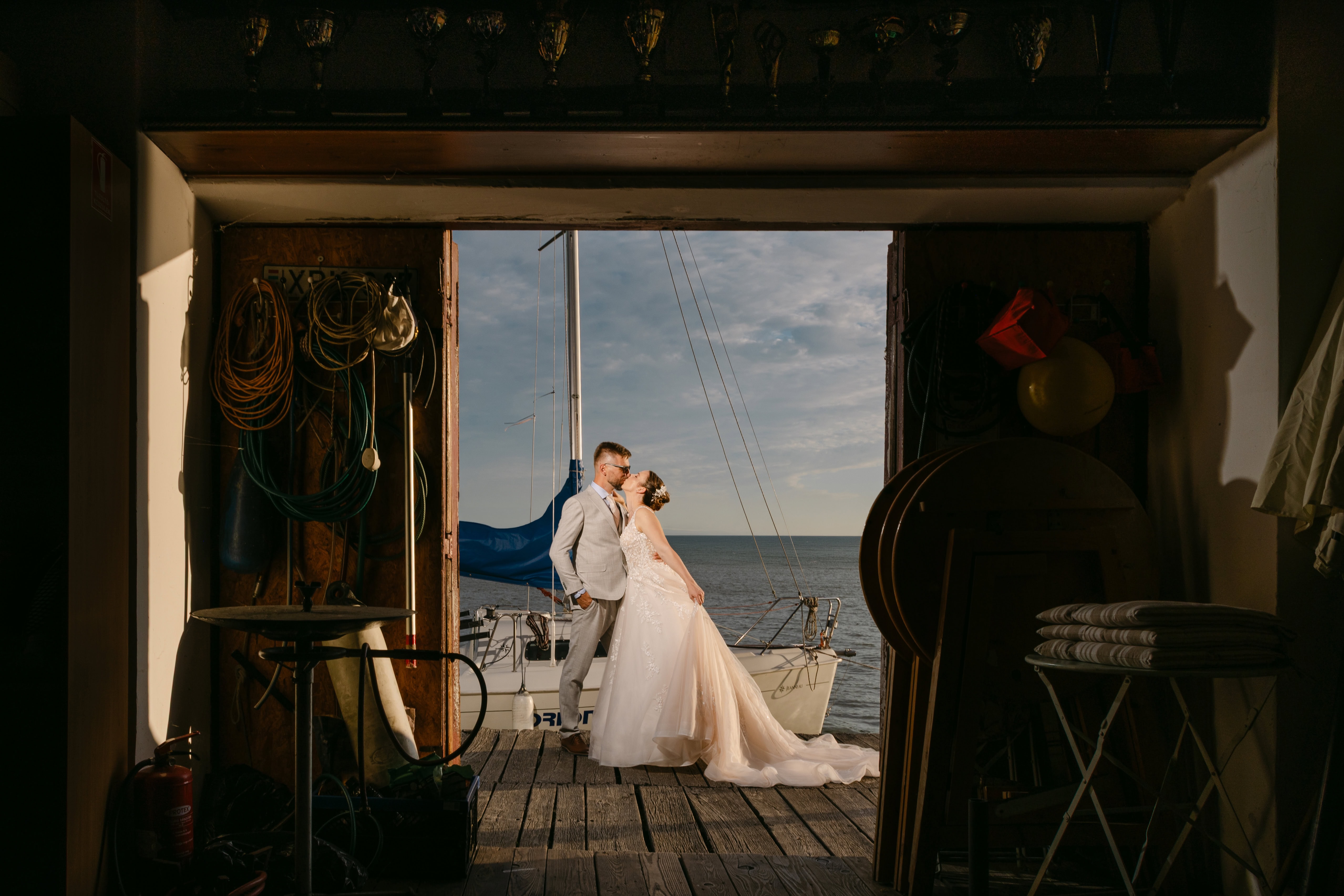 Bride and groom kissing by sailboat at sunset